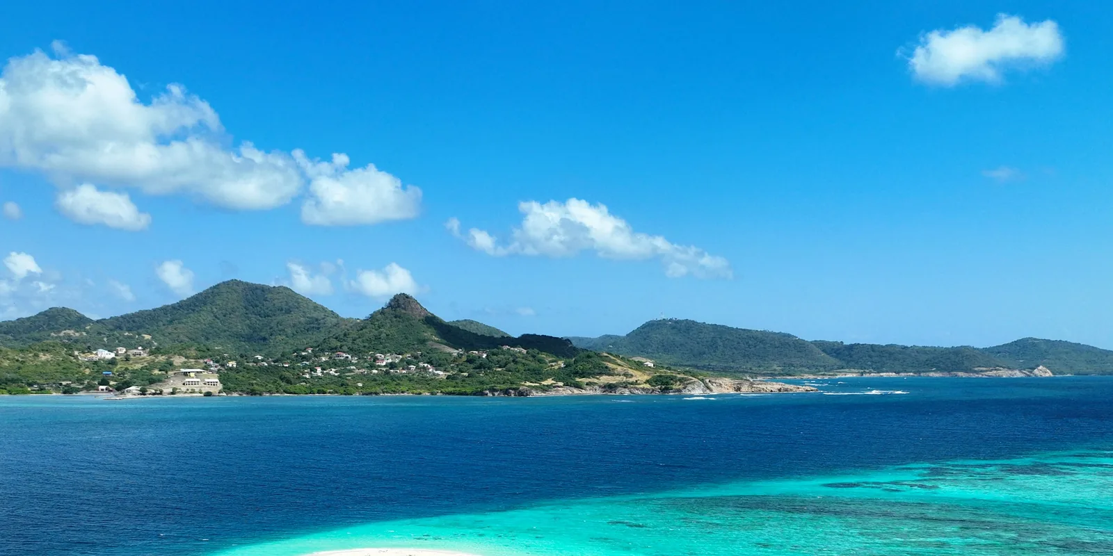 Green hills of Carriacou rising above deep blue and turquoise water in the Grenadines of Grenada